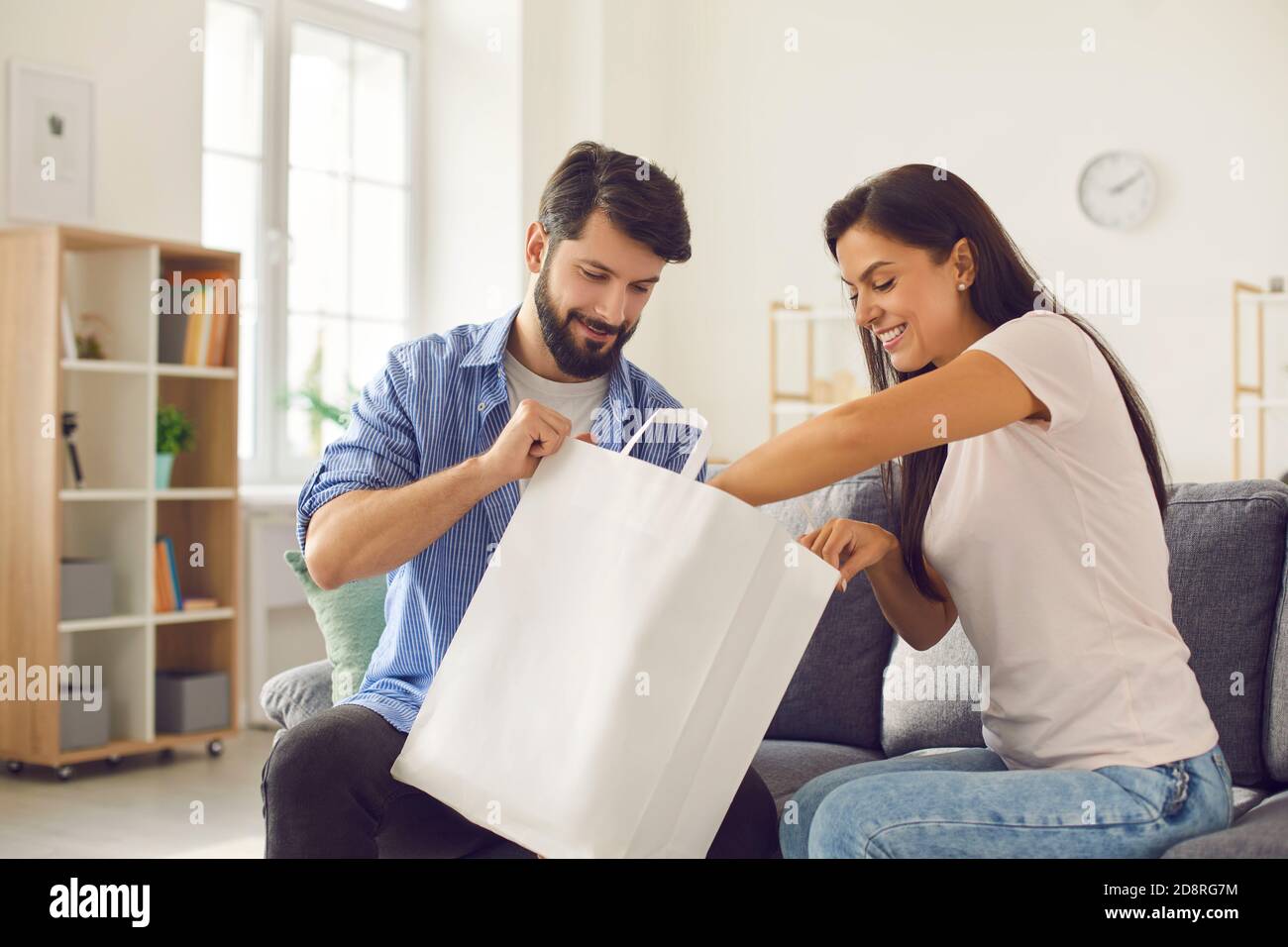 Happy young couple sitting on couch with paper bag and unpacking fresh takeaway food Stock Photo