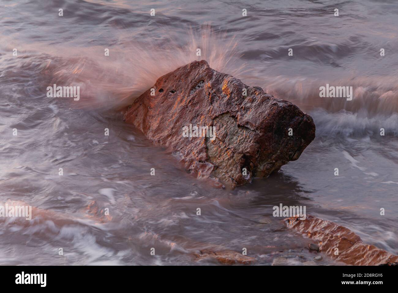 The rock catching the last of the sunlight with small wave breaking ...