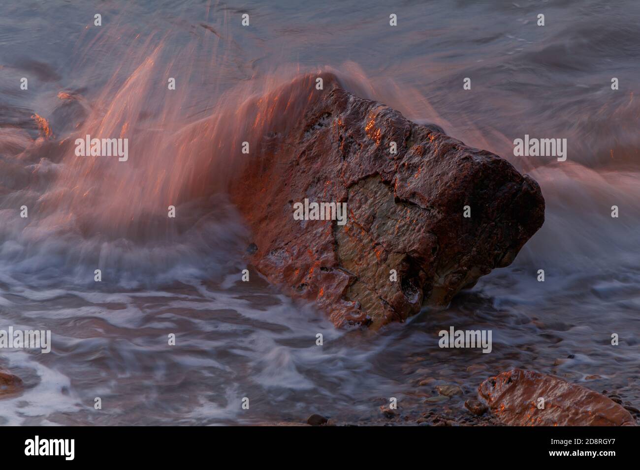 The rock catching the last of the sunlight with small wave breaking ...