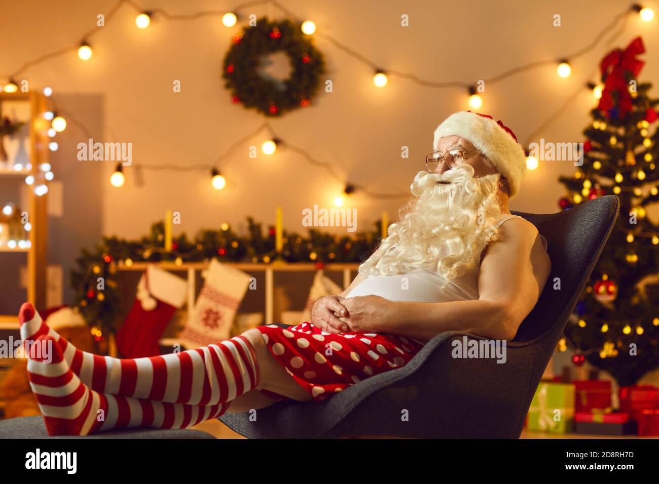 Tired Santa relaxing in comfy armchair after long workday and watching