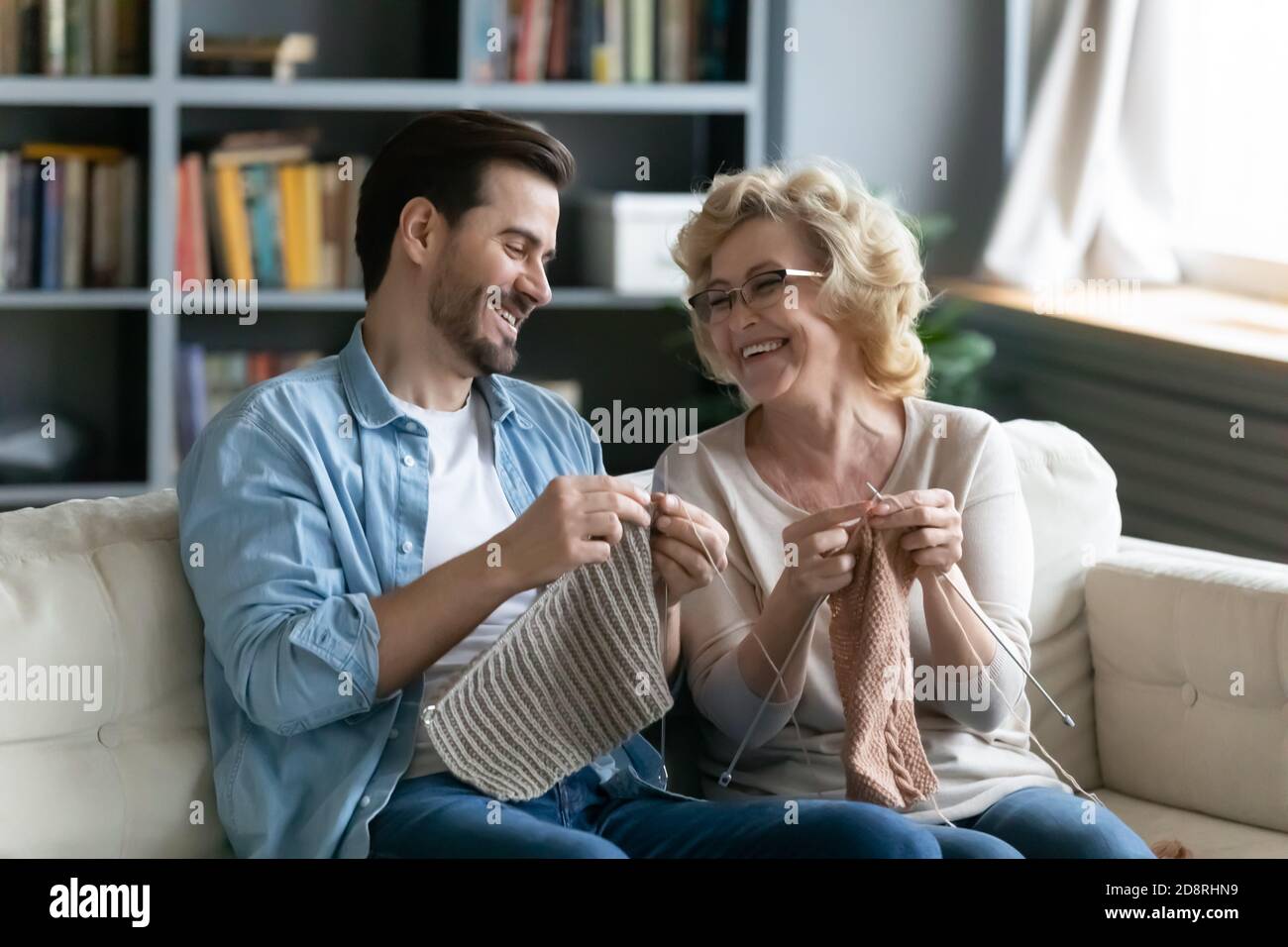 Happy young man learning needlework from smiling older mum. Stock Photo