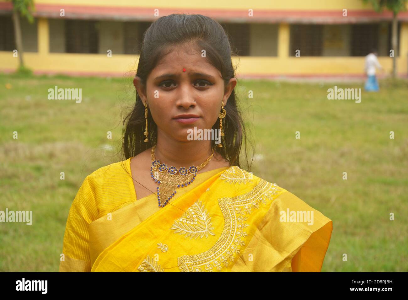 Close up of  an Indian Bengali teenage girl with long dark hairs wearing traditional yellow saree with bangles hand bag and jewelry nose ring, earring Stock Photo