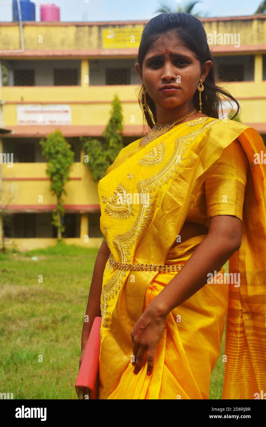 Close up of  an Indian Bengali teenage girl with long dark hairs wearing traditional yellow saree with bangles hand bag and jewelry nose ring, earring Stock Photo