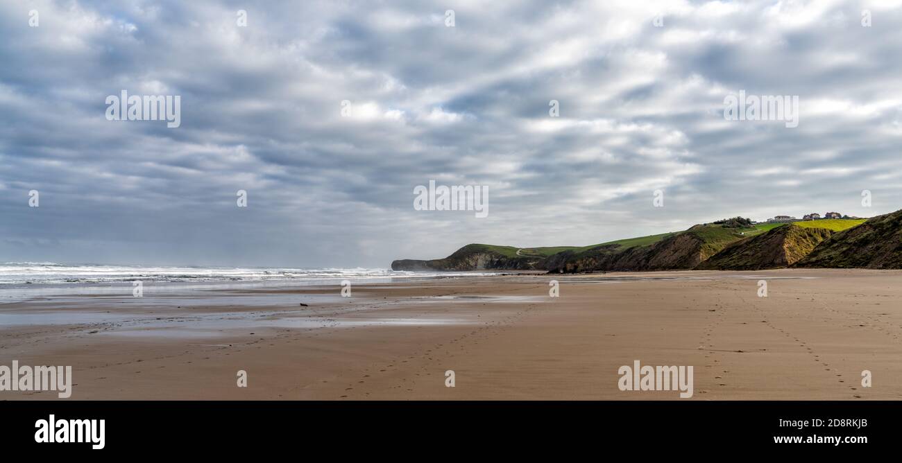 Tall green grassy cliffs drop down to the ocean coast and a large beautiful sandy beach Stock Photo