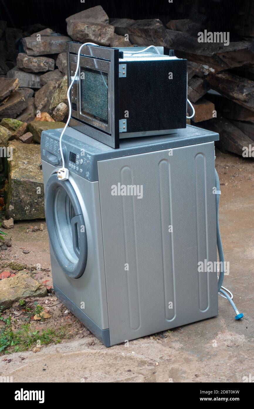Old washing machine and microwave outside home waiting for collection