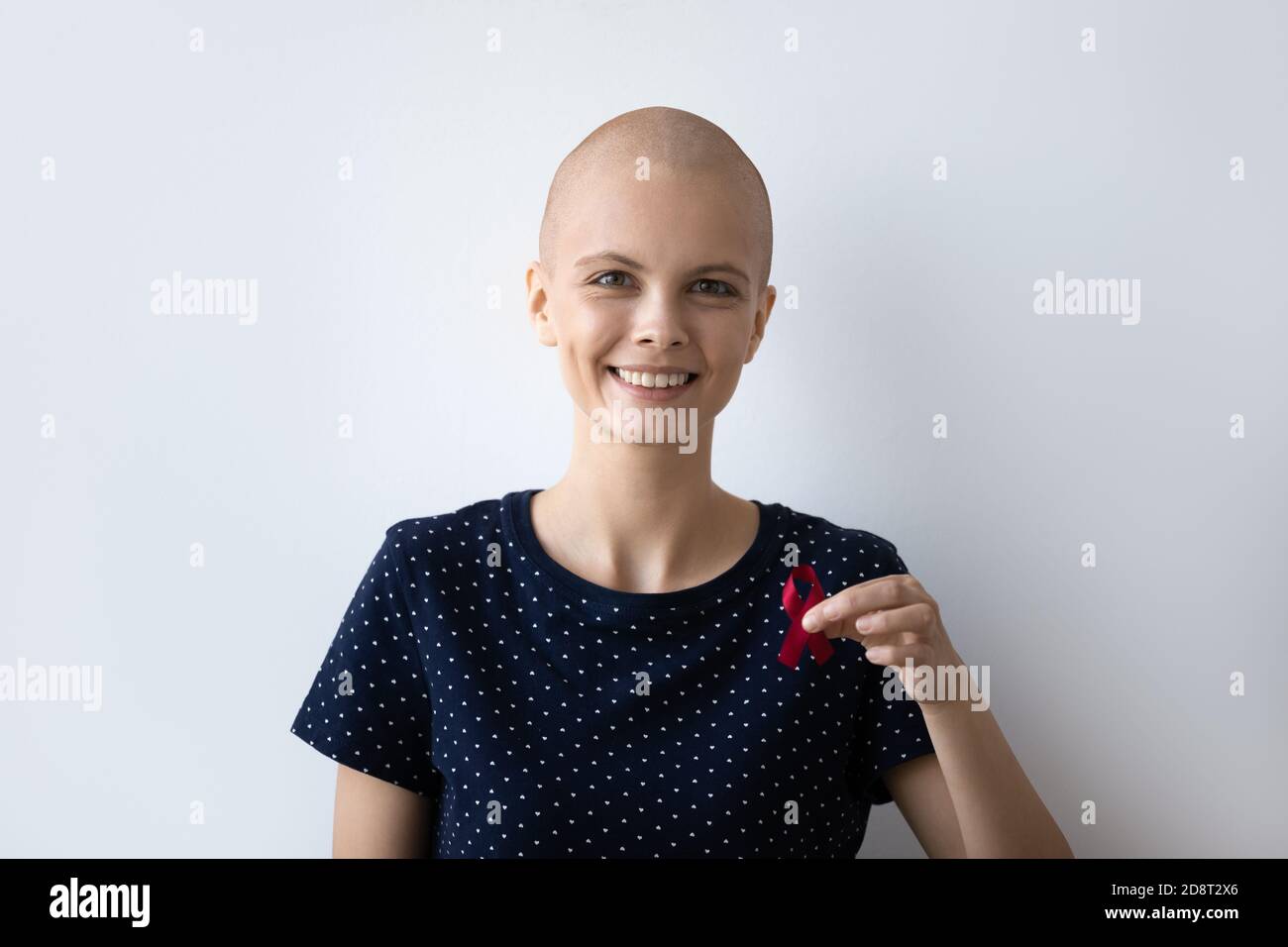 Head shot portrait smiling hairless woman holding awareness red ribbon Stock Photo