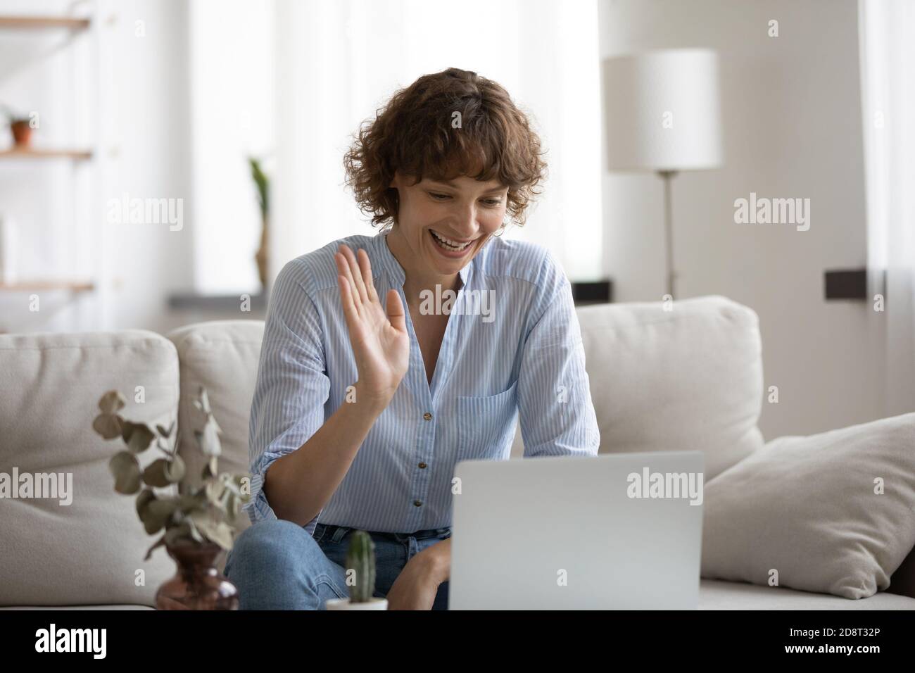 Close up smiling woman waving hand, using laptop at home Stock Photo