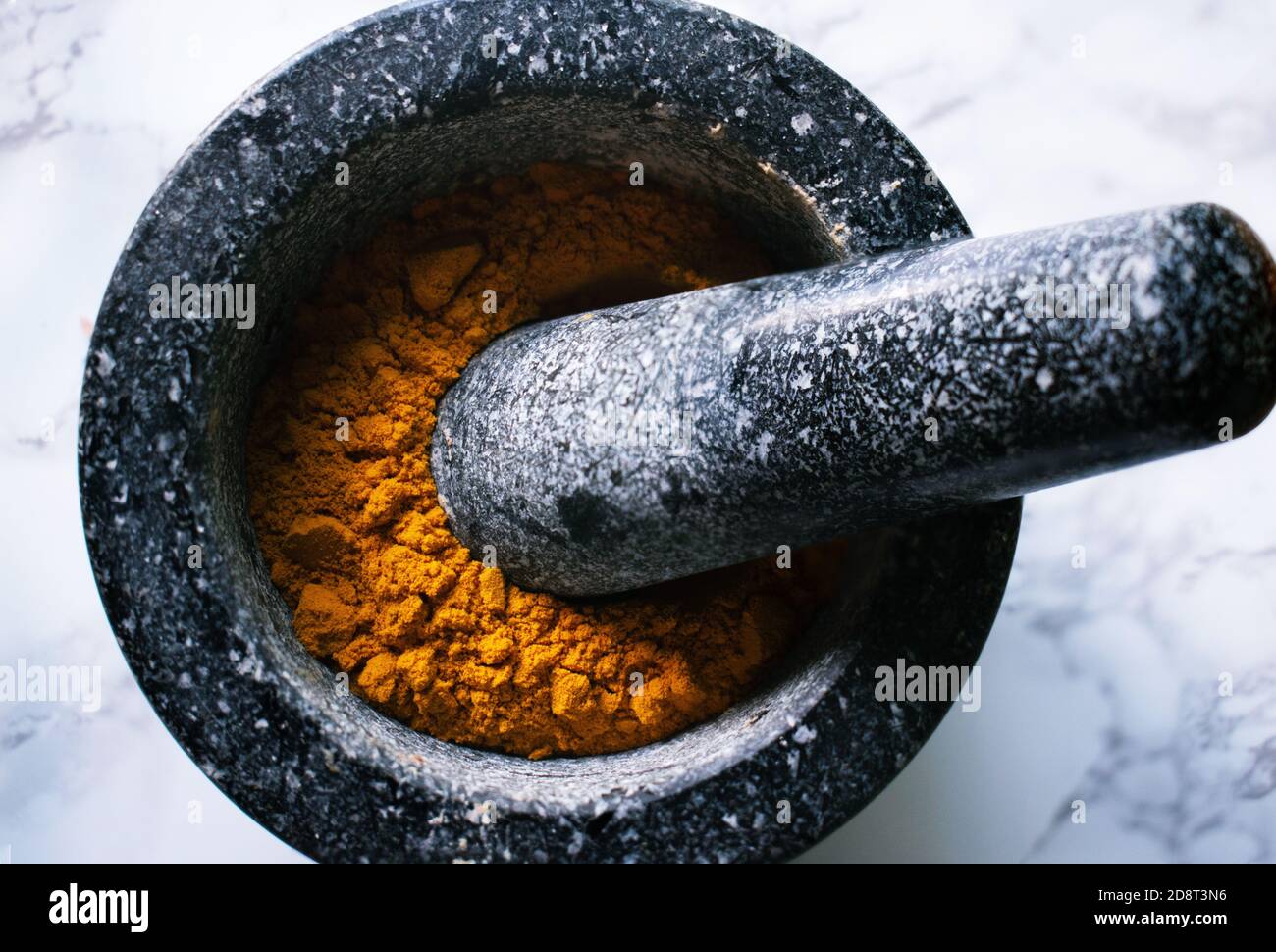 Vivid orange from Turmeric spice in dark stone mortar and pestle Stock Photo