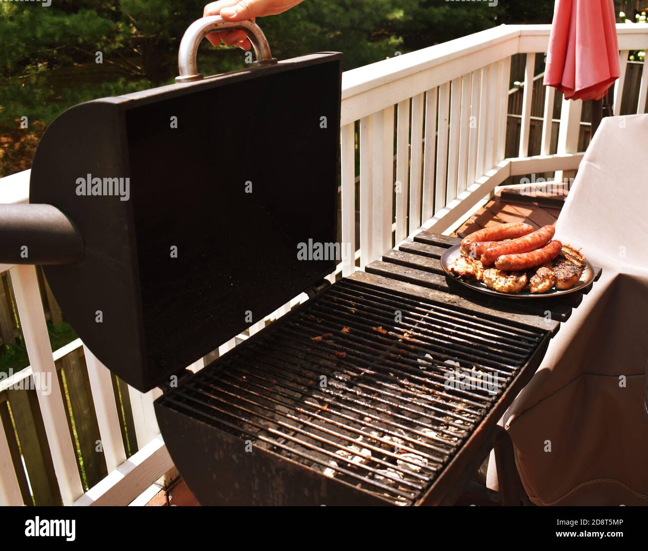 Open charcoal grill on a balcony, with a plate of cooked sausage and