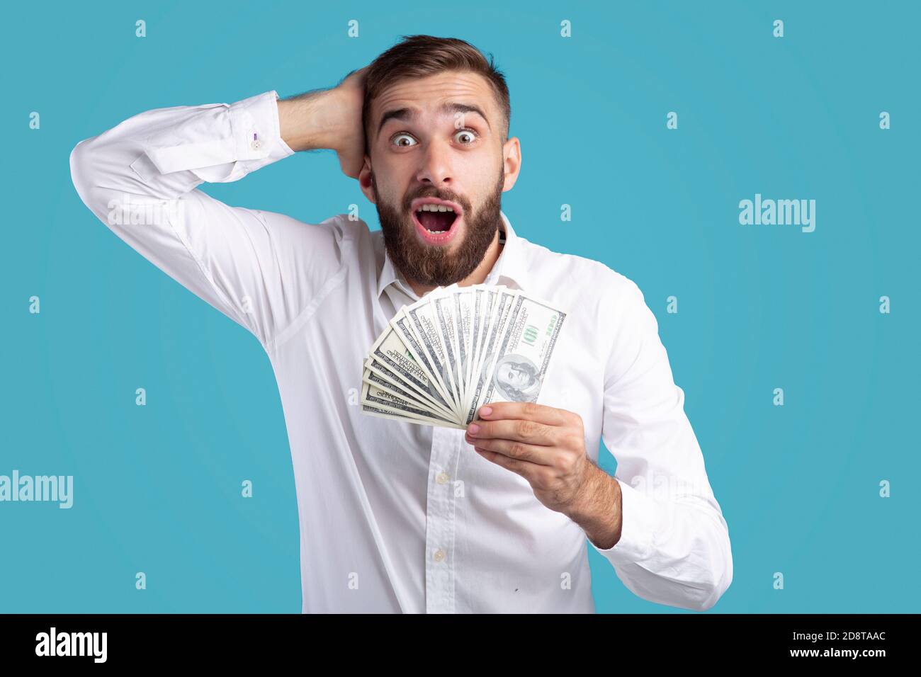 Excited Caucasian guy with fan of money touching his head in shock on ...