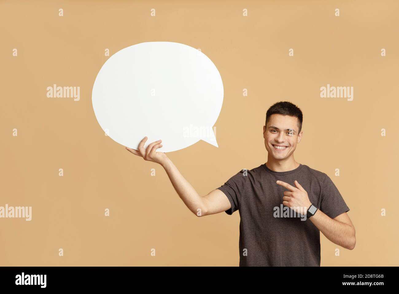 Smiling young guy with smart watch holds blank space for words in hand and points to abstract bubble Stock Photo