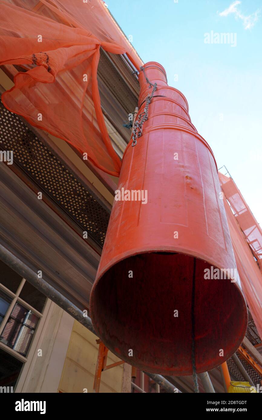 Trash chute or debris chute in red color on a facade of a historic building in reconstruction for rubbish removal. Low angle view with detail. Stock Photo