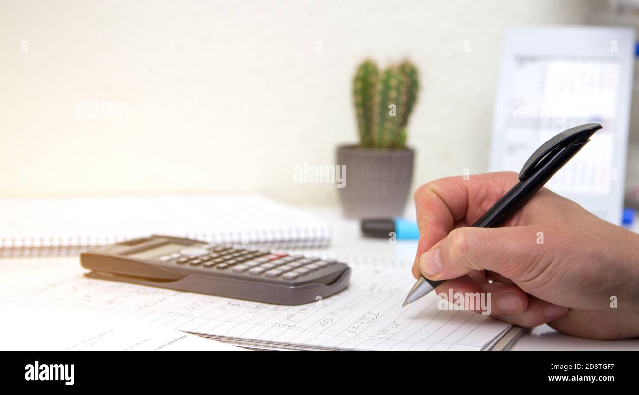 The student solves mathematical formulas. Man writes with a pen in a notebook. Homework. Notes in a notebook. Stock Photo