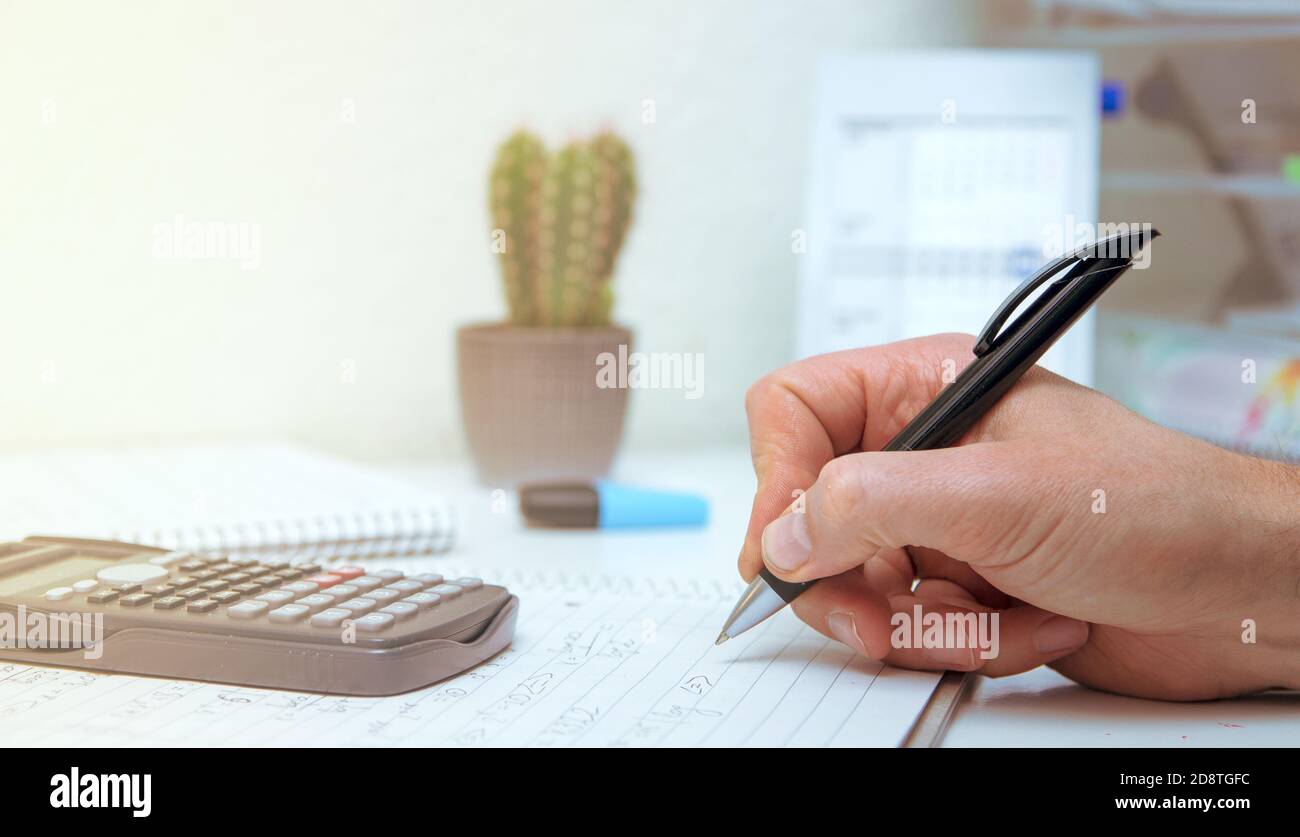 The student solves mathematical formulas. Man writes with a pen in a notebook. Homework. Notes in a notebook. Stock Photo