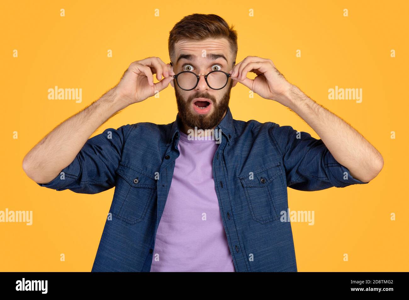 Surprised Caucasian man in casual clothes and glasses opening mouth in amazement on orange studio background Stock Photo
