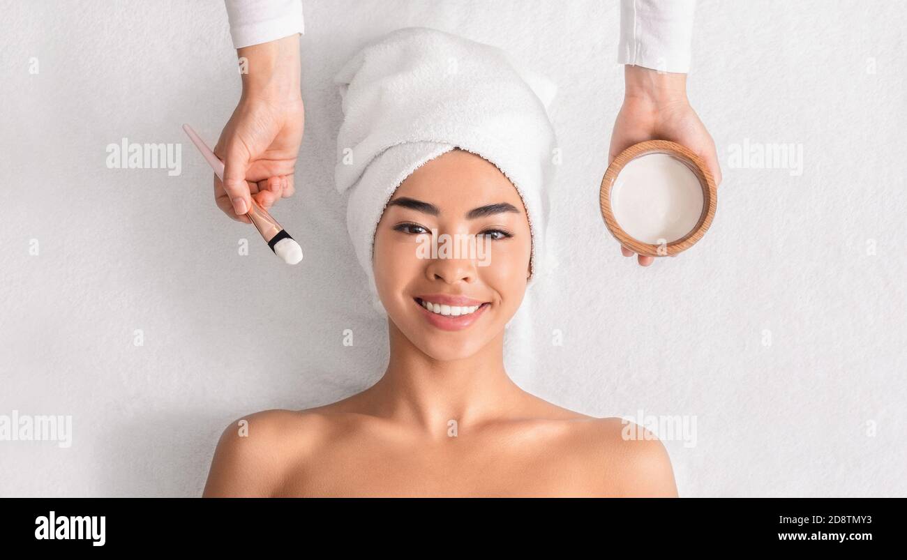 Facial Treatment. Cosmetologist applying clay mask on asian woman's face at spa Stock Photo