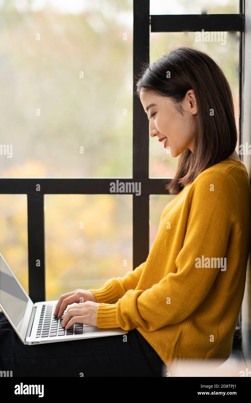 Asian woman working on laptop at home or in cafe on window. Stock Photo