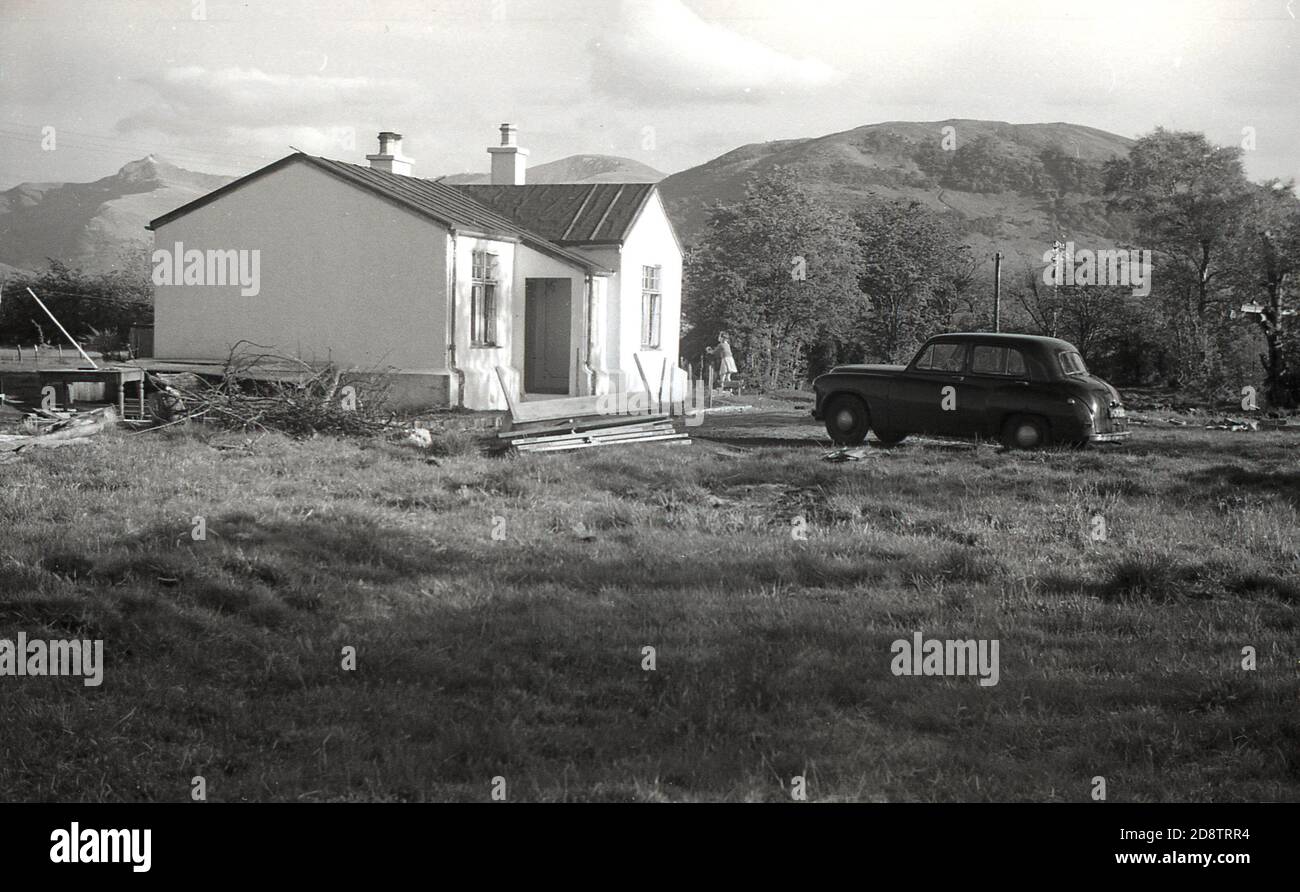 1950s, historical, a single-storey building, a bungalow being constructed in the foot of the Snowdonia, mountains, Wales, with a car of the era and a young girl outside the building. Stock Photo