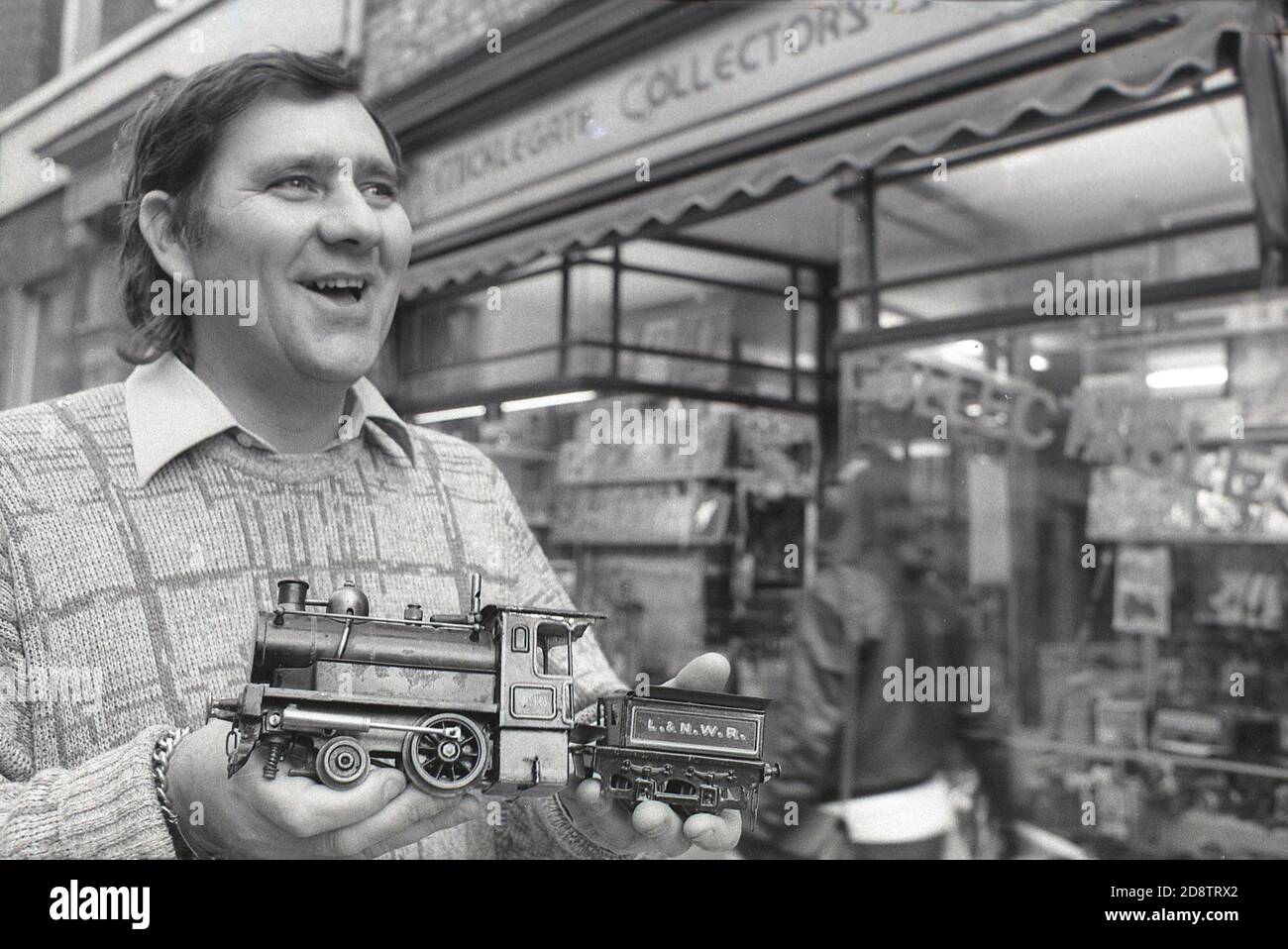 1980s, historical, outside a model train and collectors shop in Micklegate Street, York, England, UK, a man proudly holding a model of an L & N W R steam locomotive and wagon. Model railways are a popular hobby and those who collect model trains are known as rail enthusiasts. The Englsih city of York is home to the National Railway Museum, where world-changing inventions such as the Rocket and the Mallard, the world's fastest steam locomotive, are located. Stock Photo