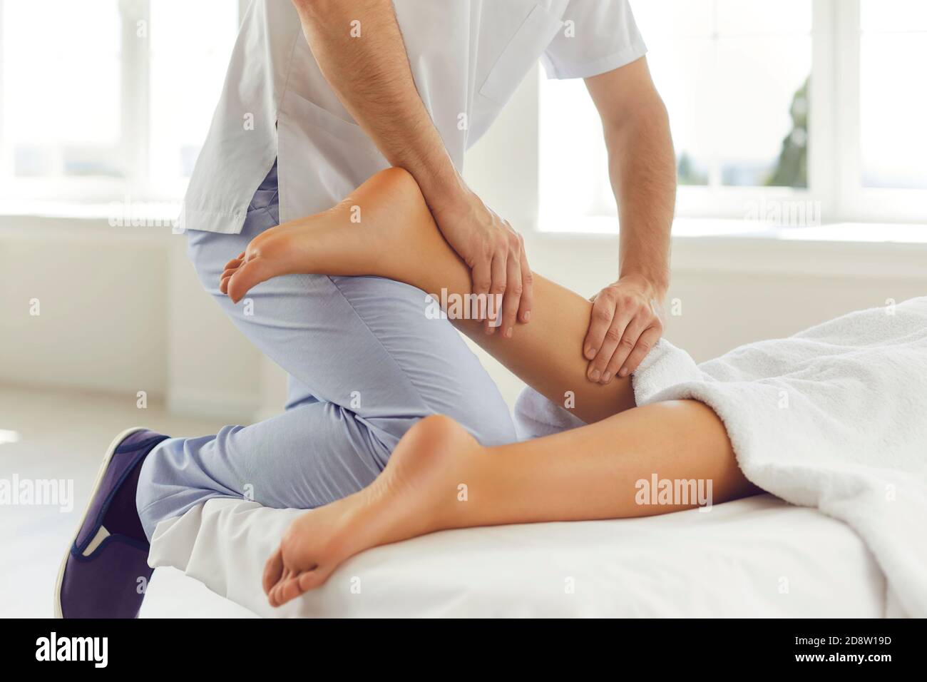 Physiotherapist or reflexologist massaging young woman's calf muscle in wellness center Stock Photo