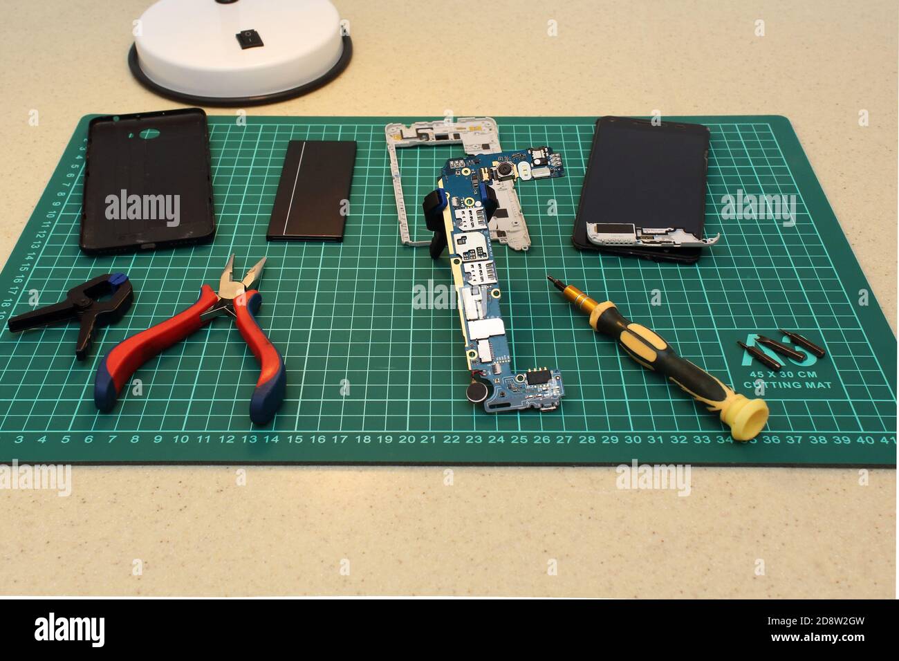 Mobile phone service. Close-up of  repairing smartphone with screwdriver, pliers and clamp on green pad. Stock Photo