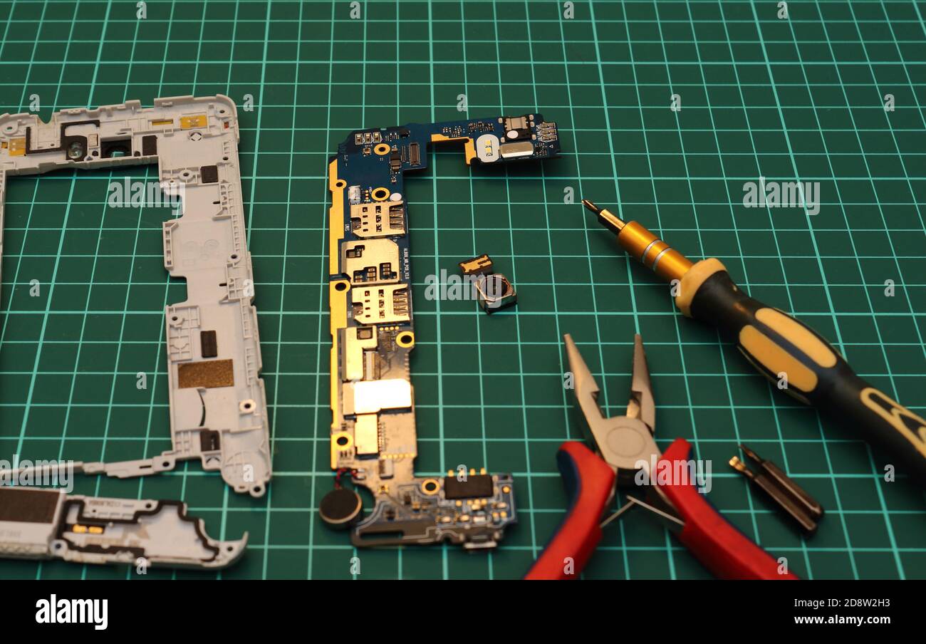 Mobile phone service. Close-up of  repairing smartphone with screwdriver and pliers on green pad. Stock Photo