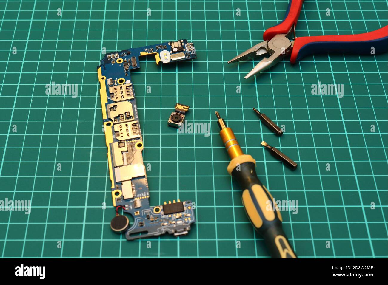 Mobile phone service. Close-up of  repairing smartphone with screwdriver and pliers on green pad. Stock Photo