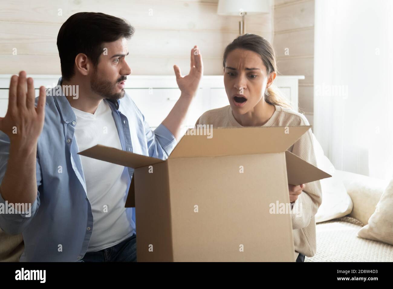 Confused shocked millennial spouses opening delivery with spoiled defective goods Stock Photo