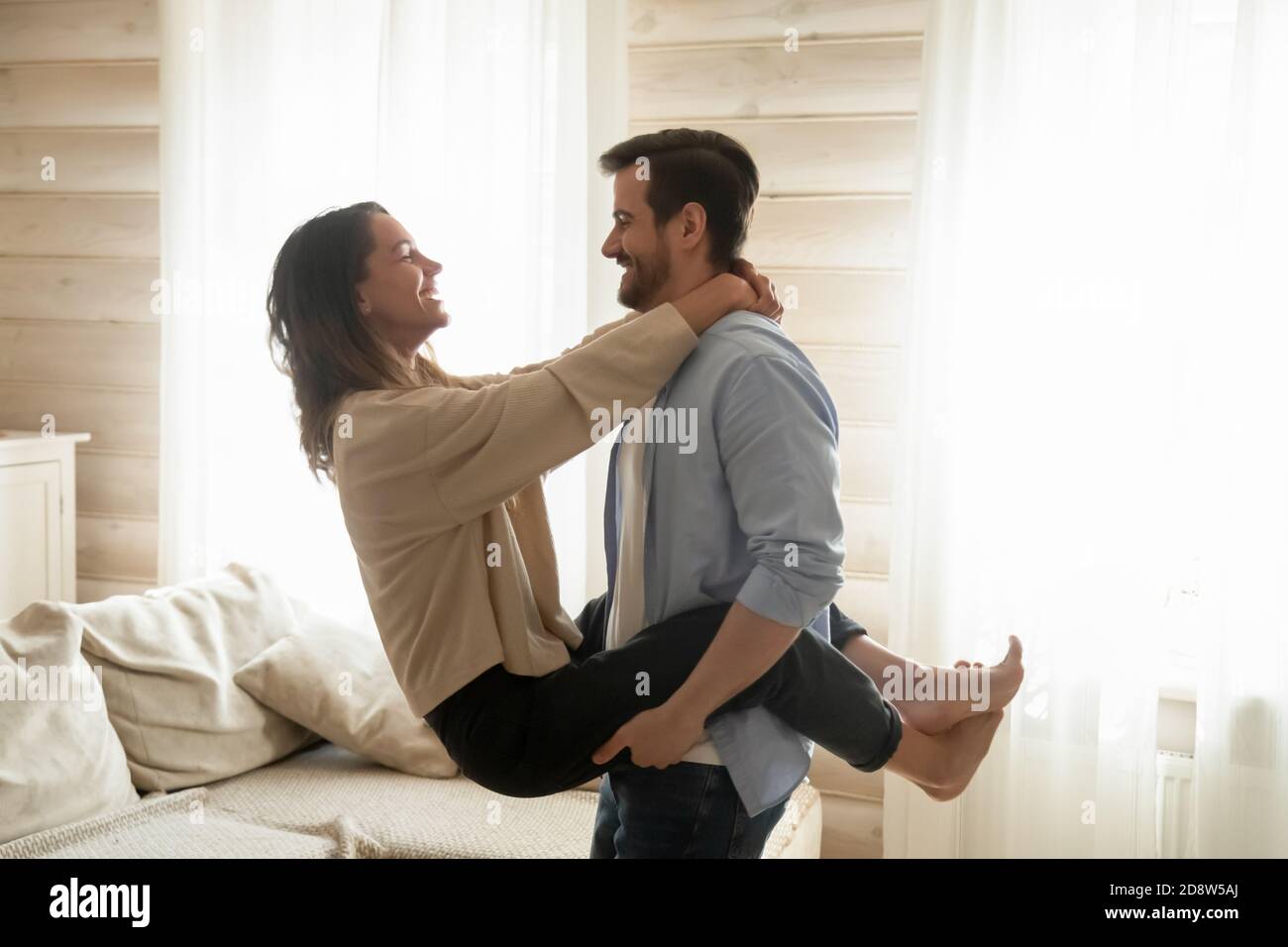 Affectionate boyfriend holds smiling girlfriend in arms lifting in air
