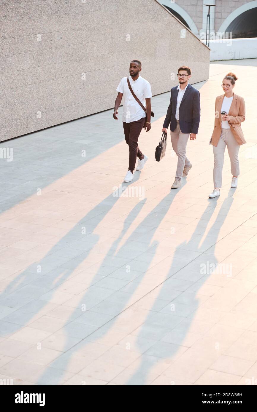 Group of young managers moving along tiled marble wall of modern building Stock Photo