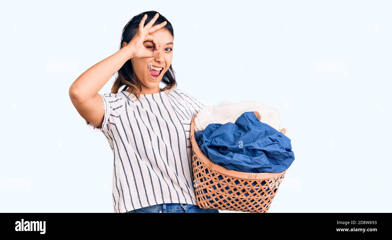 Young woman holding laundry basket smiling happy doing ok sign with ...