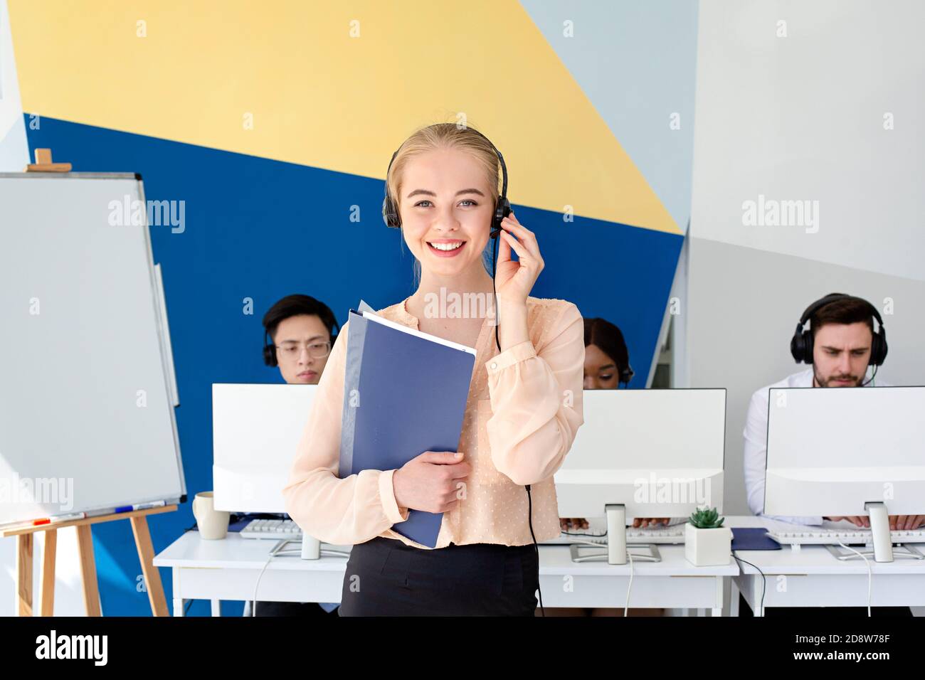 Attractive female hotline operator looking at camera and smiling in modern office Stock Photo