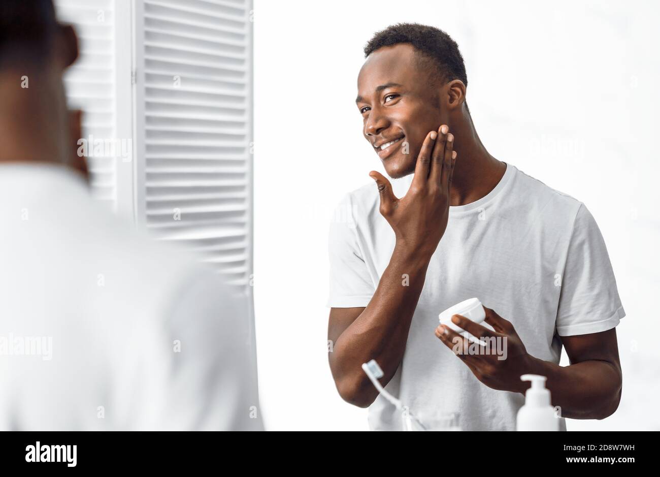 Black Man Using Facial Cream Moisturizing Face Skin In Bathroom Stock