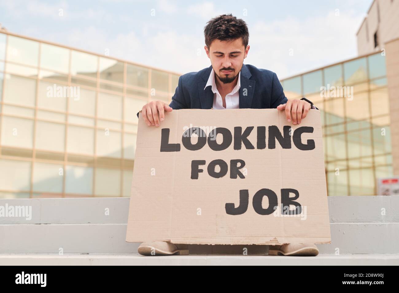Young frustrated man looking at piece of cardboard with notice of needing job Stock Photo
