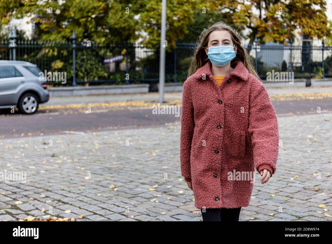 Blonde girl in pink winter coat walking with confidence on a city street wearing a face mask for Corona virus pandemic. Stock Photo