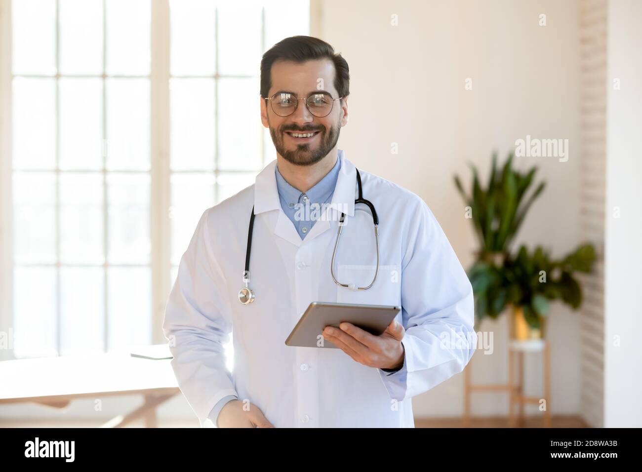 Portrait of happy confident young male doctor with tablet pc Stock Photo