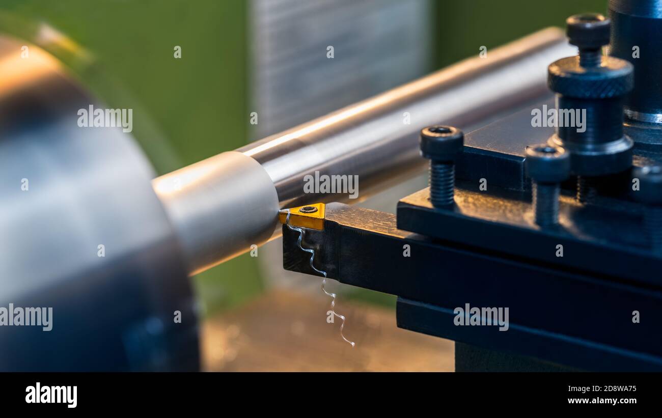 Lathe turning of cylindrical duralumin workpiece by sharp cutting tool bit. Closeup of working machine with yellow carbide knife in black metal holder. Stock Photo