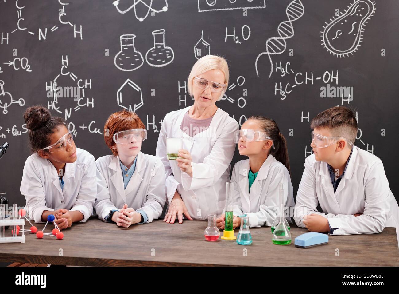 Young teacher of chemistry and group of pupils discussing chemical reaction Stock Photo