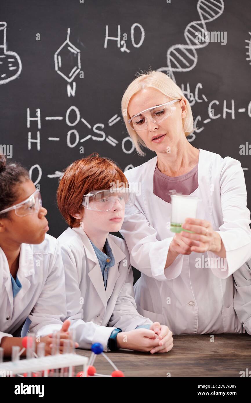 Teacher of chemistry in whitecoat showing intercultural pupils chemical mixture Stock Photo