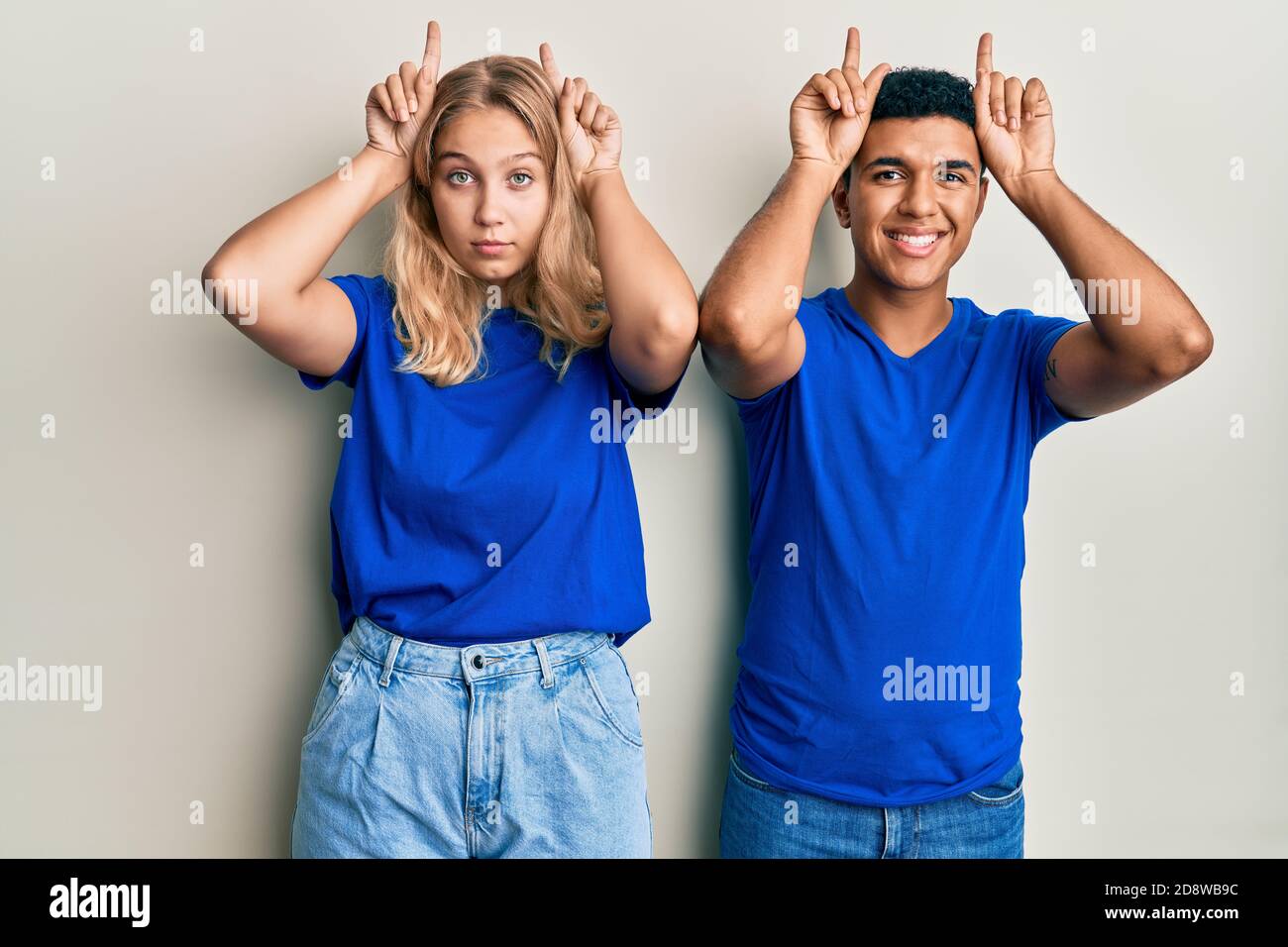 Young interracial couple wearing casual clothes doing funny gesture with finger over head as bull horns Stock Photo
