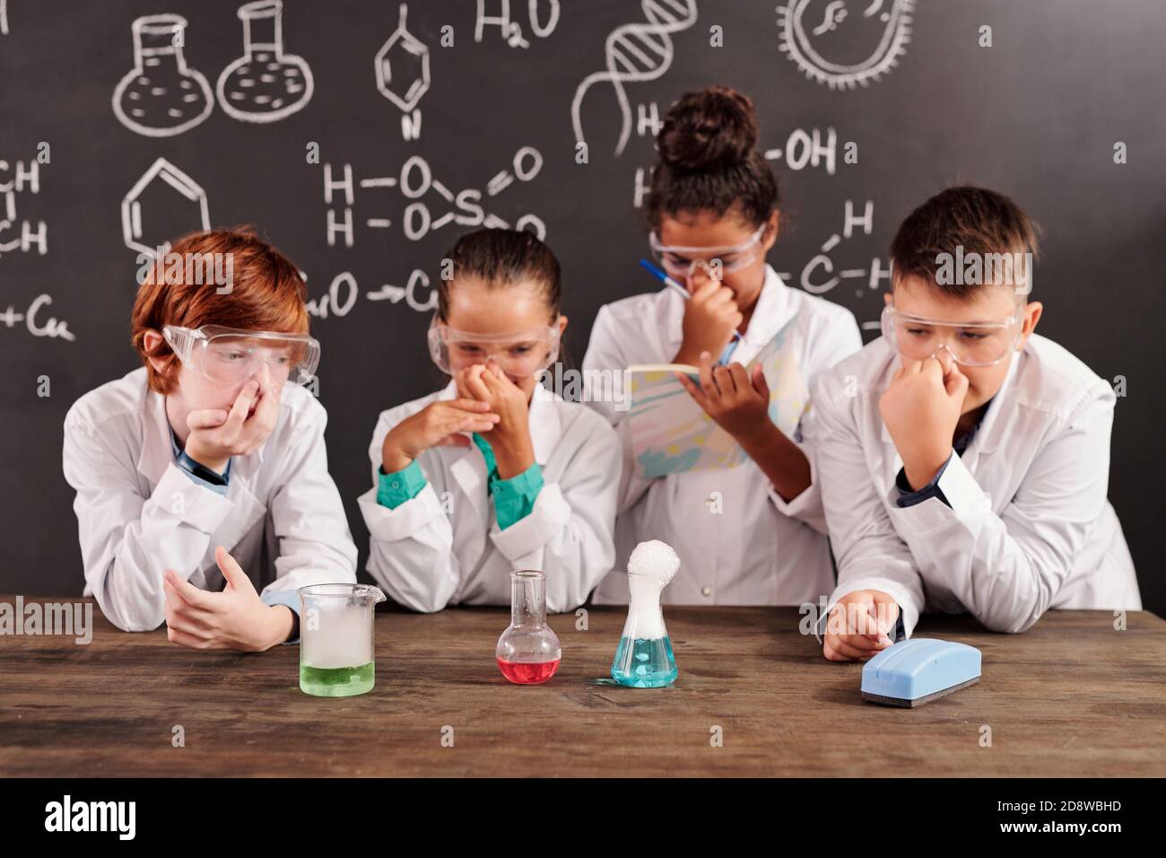 Cute schoolkids in protective eyeglasses plugging noses while watching reactions Stock Photo
