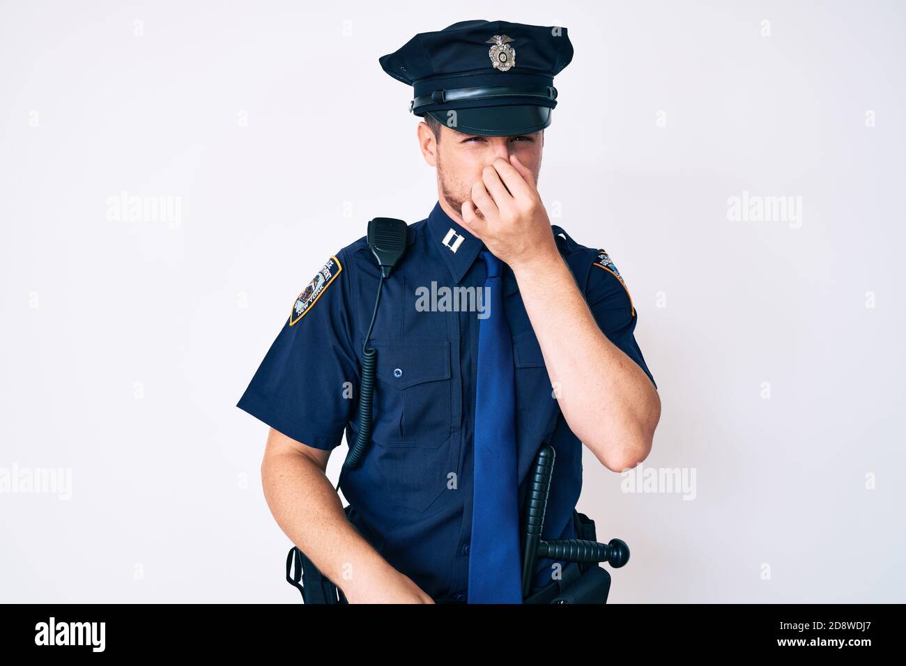 Young caucasian man wearing police uniform smelling something stinky ...