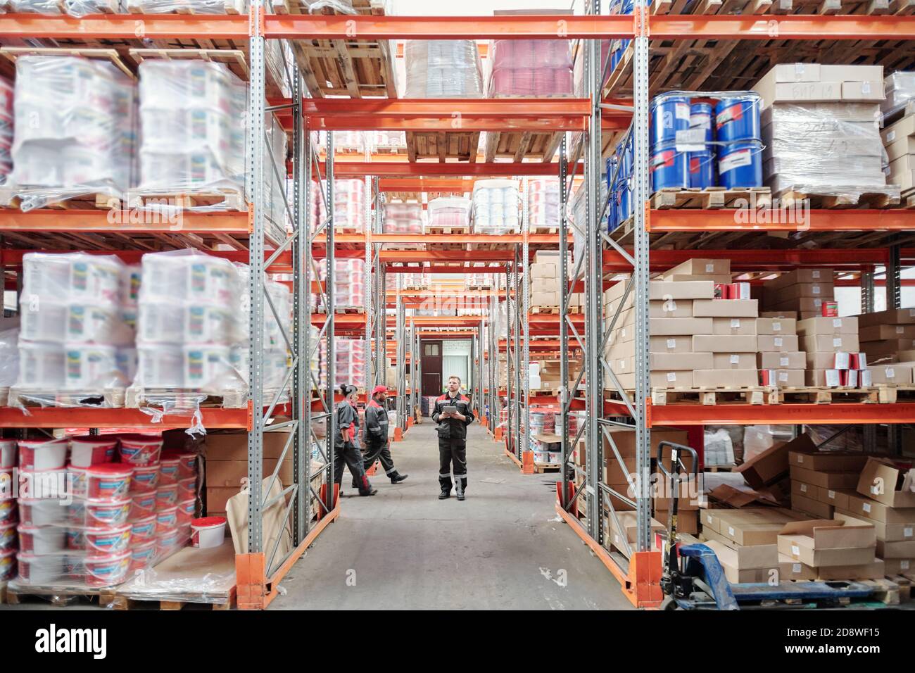 Young intercultural warehouse workers in uniform moving along large racks Stock Photo