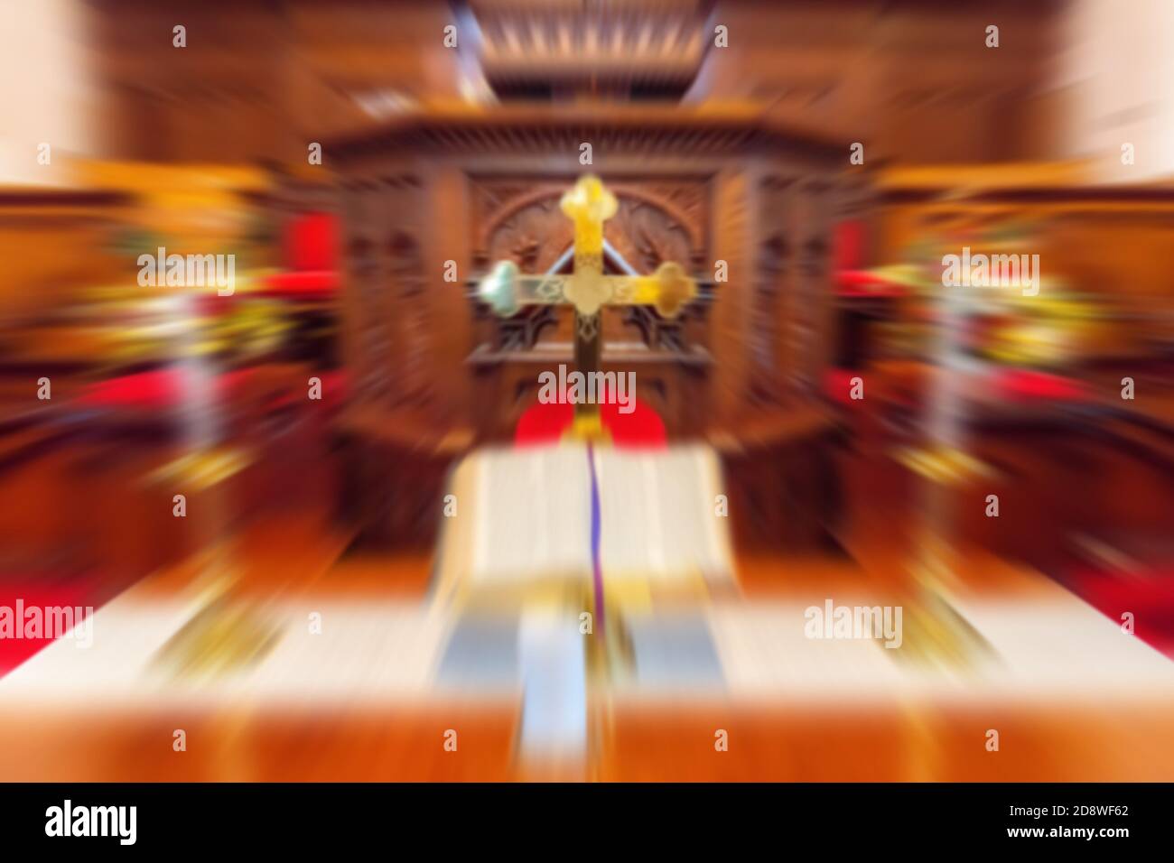 A radial blur of a church altar. The blur radiates from the crucifix on the altar. Color is mainly brown, white, and red. Stock Photo