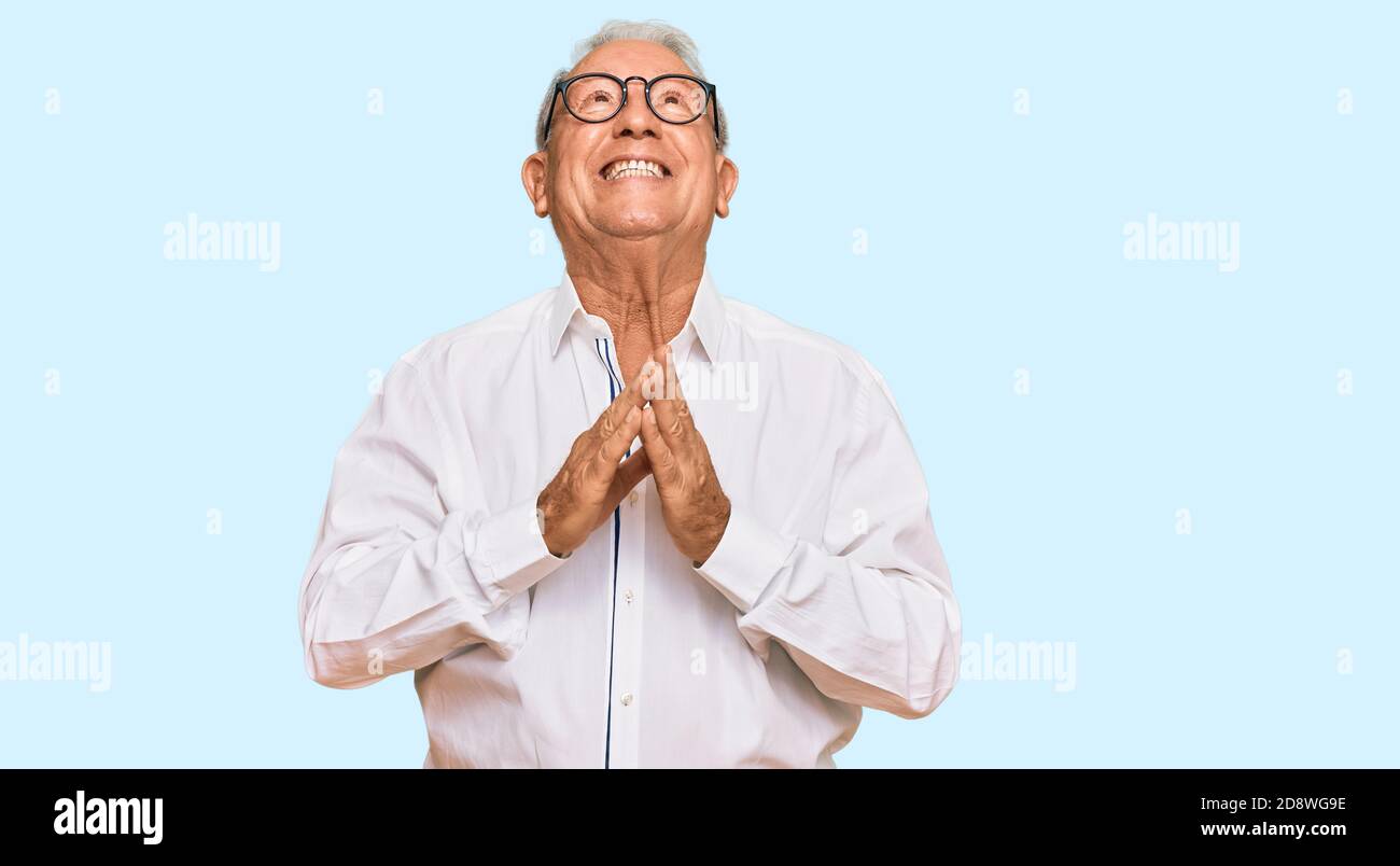 Senior caucasian man wearing business shirt and glasses begging and praying with hands together with hope expression on face very emotional and worrie Stock Photo