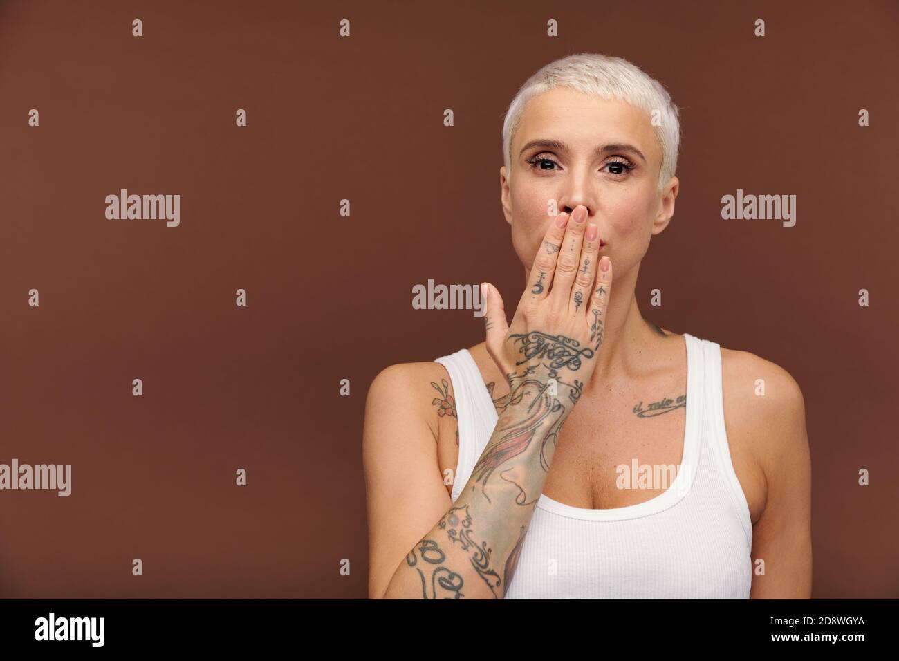 Manlike woman in white vest covering mouth by hand and showing arm with tattooes Stock Photo