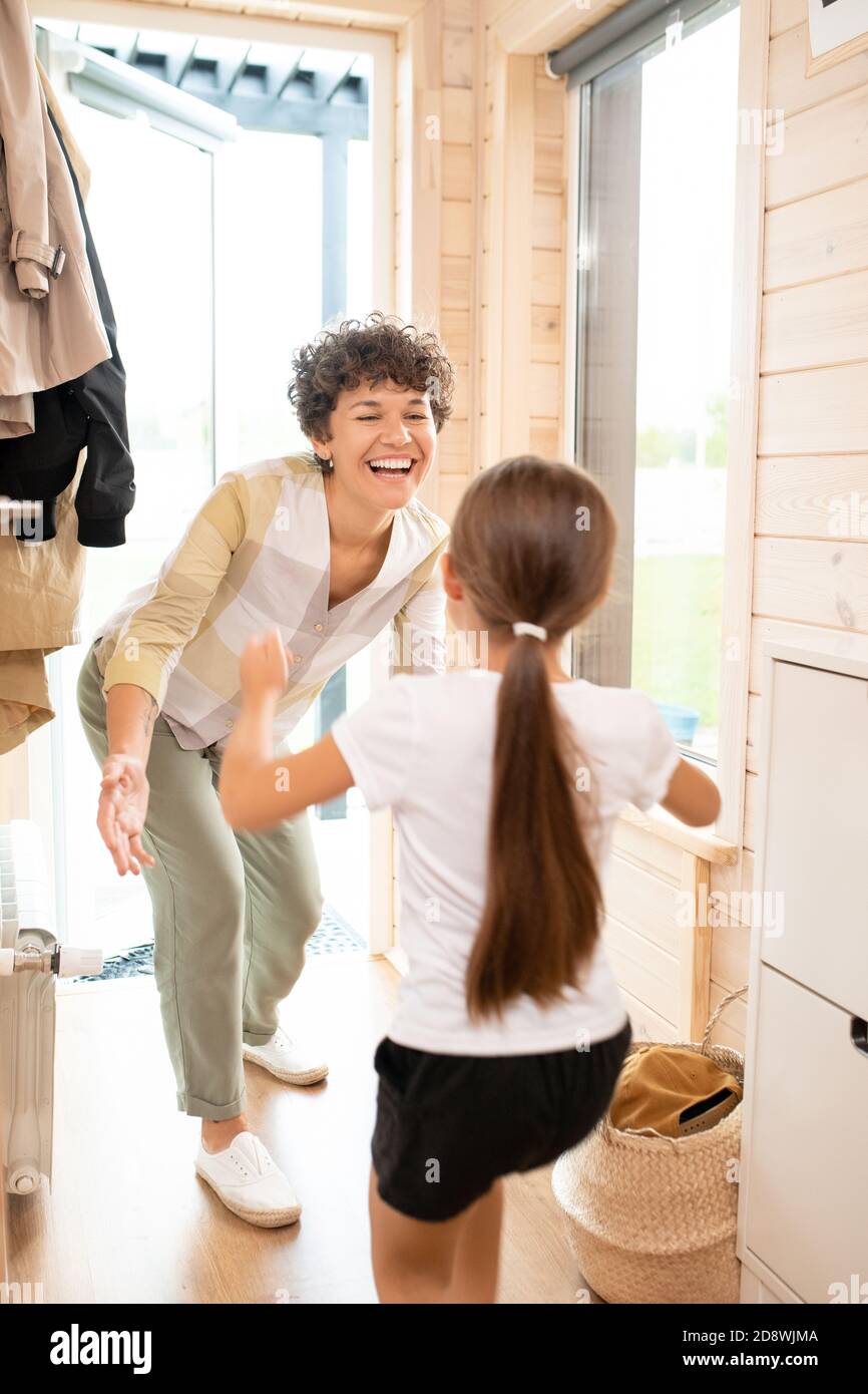 Young laughing mother standing in corridor while going to embrace her daughter Stock Photo