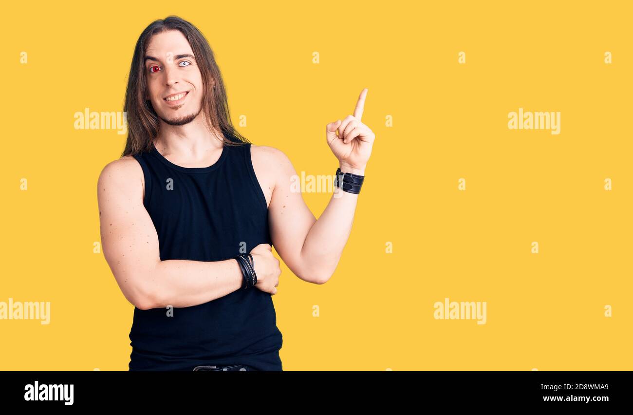 Rocking Pointing Young adult man with long hair wearing rocker style with black clothes ...