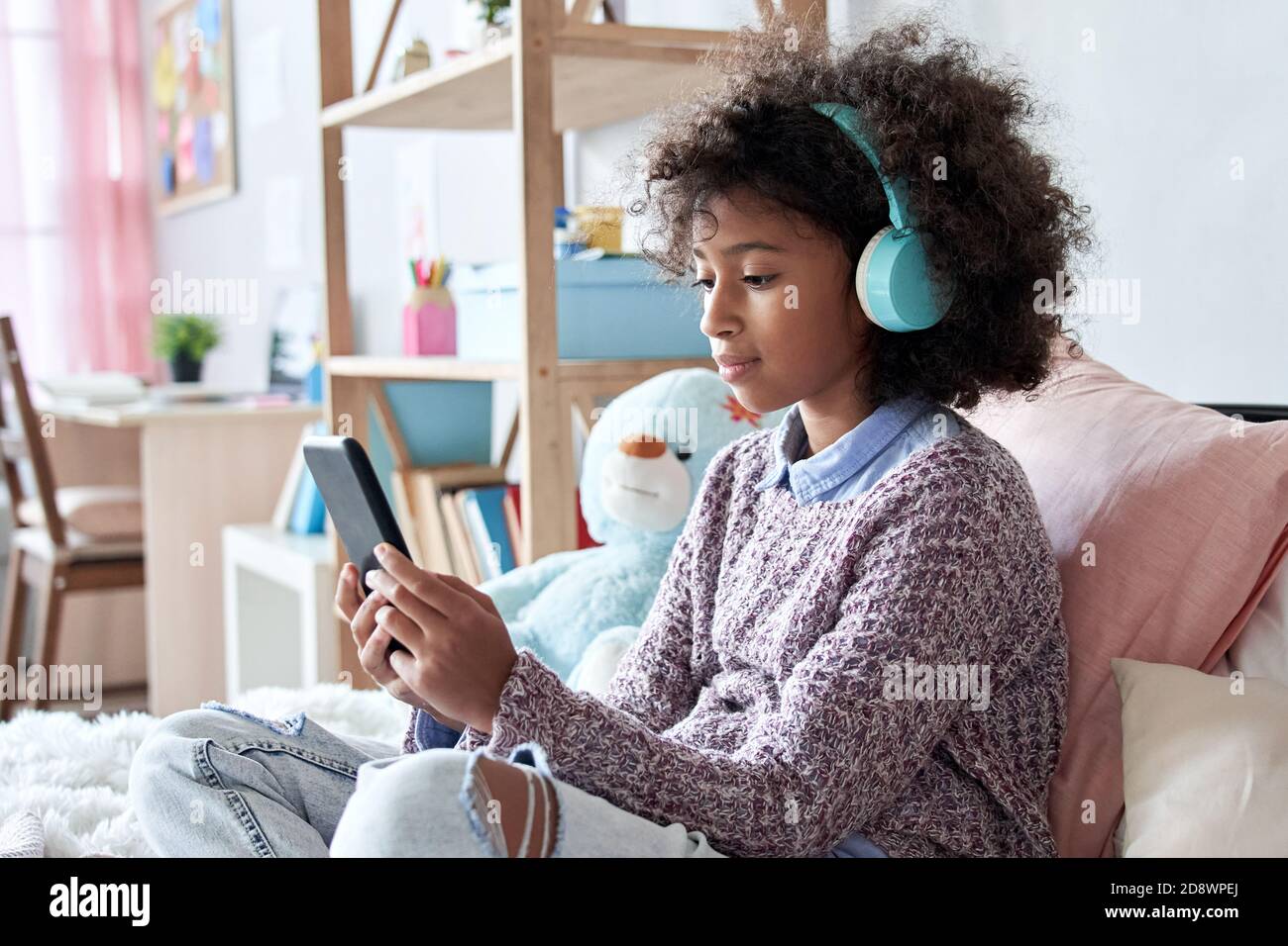 African child girl wearing headphones watching video on phone sitting on  bed Stock Photo - Alamy