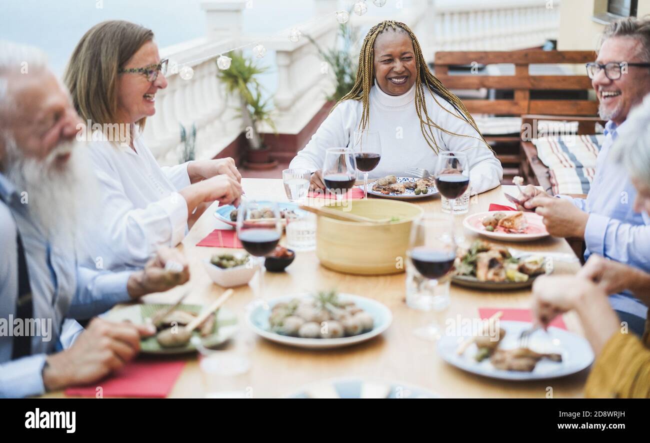 Senior multiracial people having fun at patio dinner - Happy friends eating at sunday meal - Focus on african woman Stock Photo